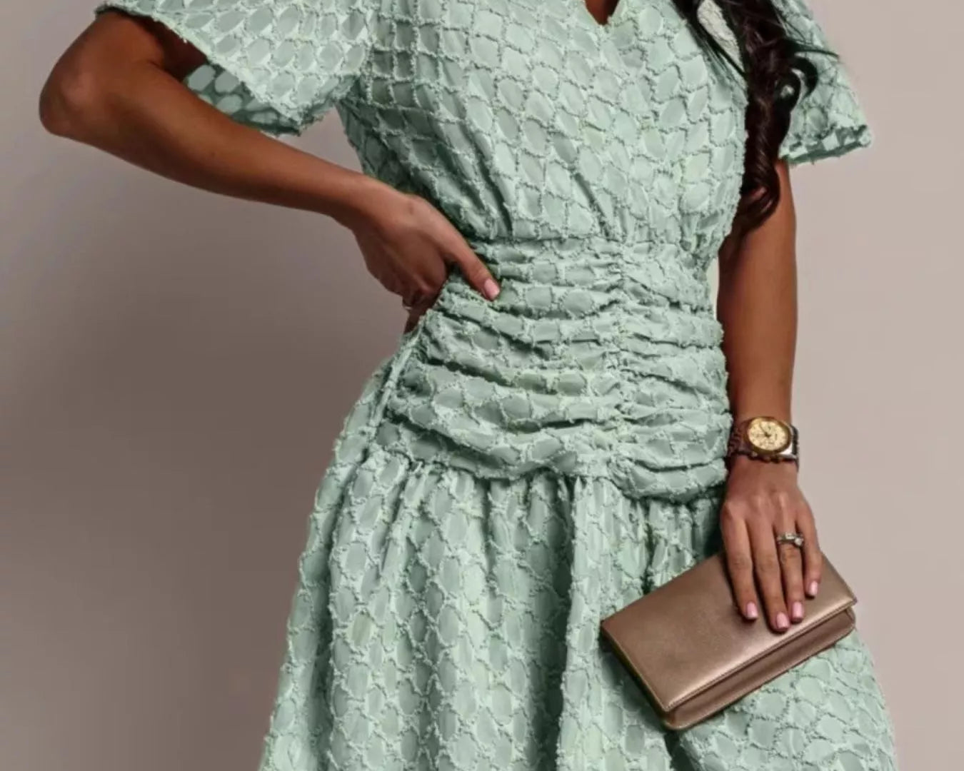 NEWYORKLISTED STYLE COLLECTION: Woman wearing a light green dress with a textured pattern, holding a clutch against a neutral background.