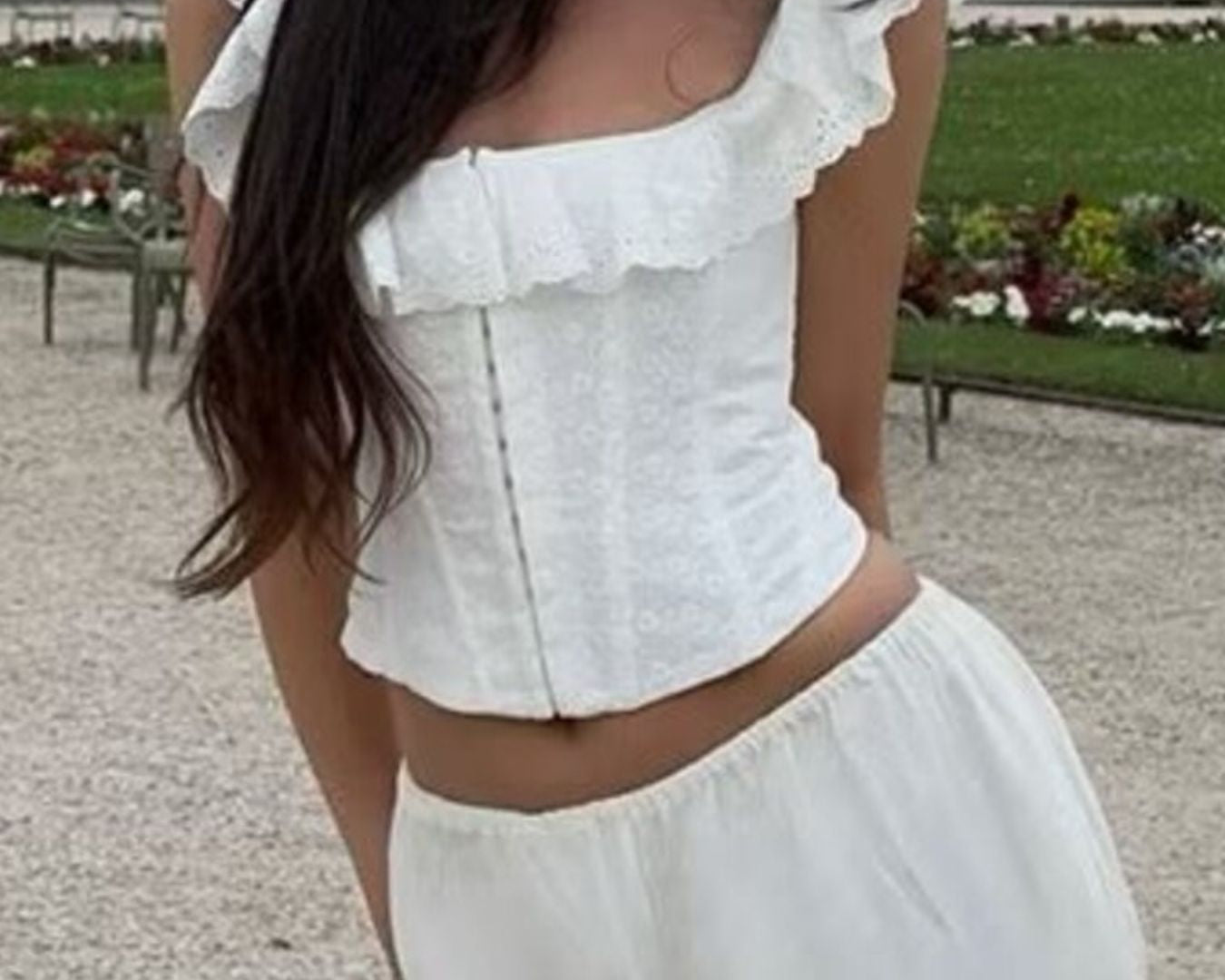 NEWYORKLISTED STYLE COLLECTION: Person wearing a white ruffled top and pants in an outdoor setting with greenery.