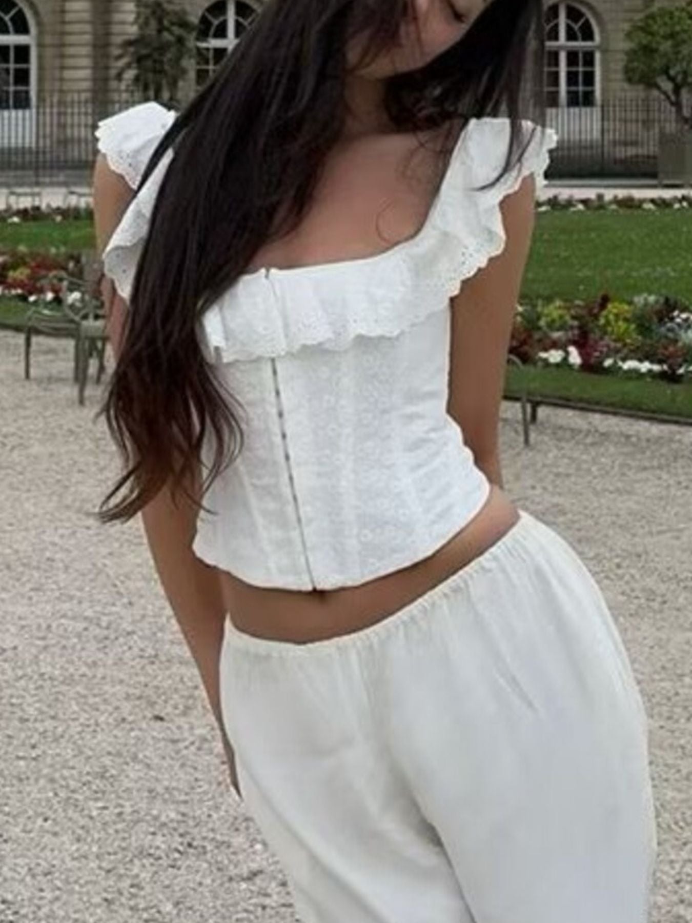 NEWYORKLISTED STYLE COLLECTION: Person wearing a white ruffled top and pants in an outdoor setting with greenery.