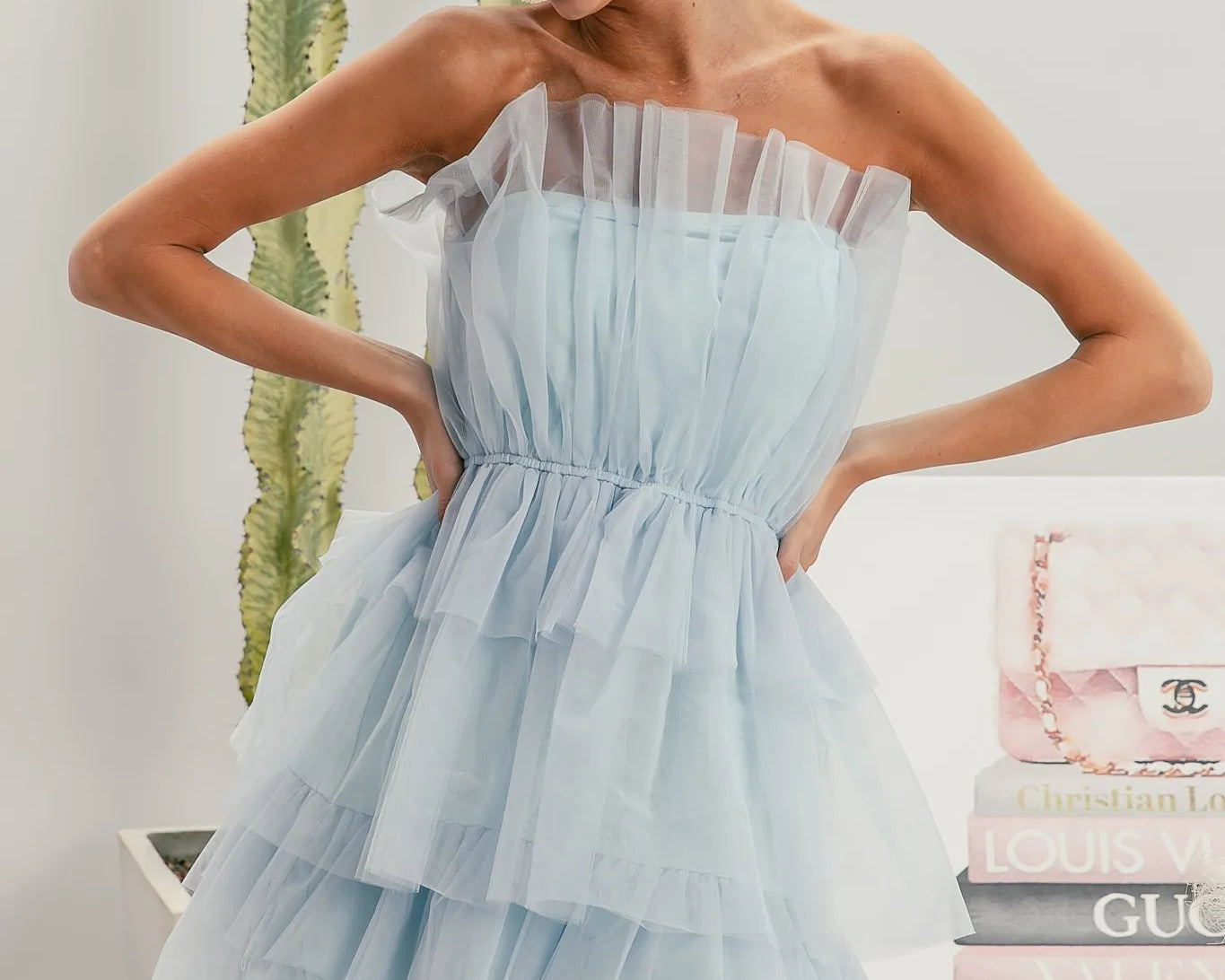 Woman wearing a light blue strapless dress with sunglasses and earrings, standing in front of a stack of fashion magazines.