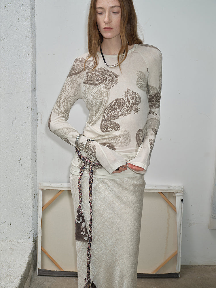 NEWYORKLISTED STYLE COLLECTION: Woman wearing a long-sleeve top with intricate patterns standing against a plain wall.