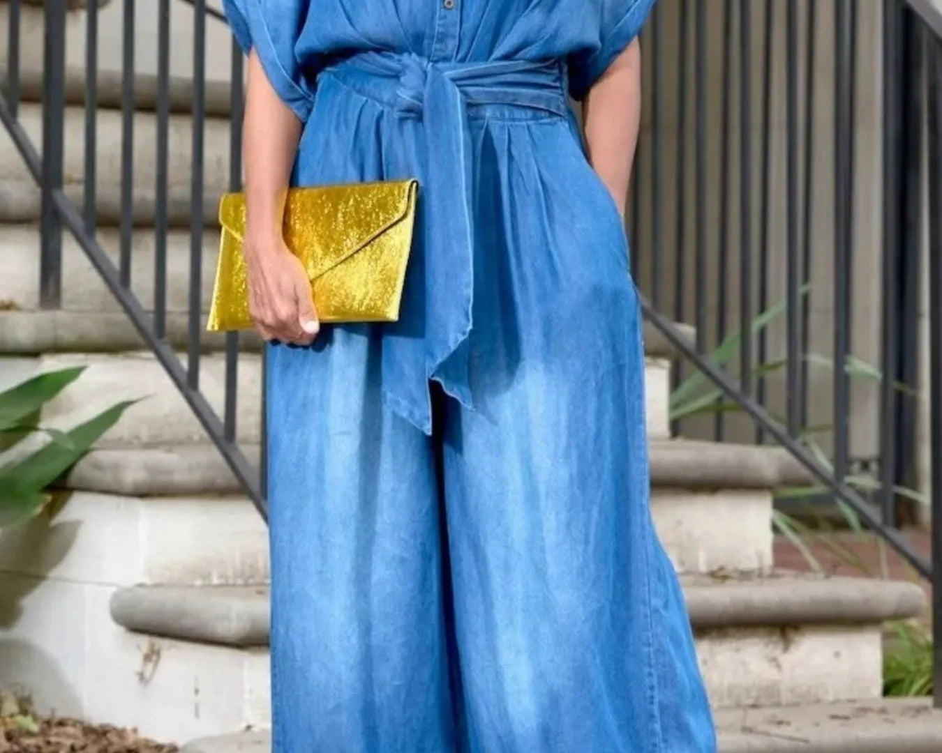 NEWYORKLISTED STYLE COLLECTION: Person wearing a blue outfit with wide-leg pants and a yellow clutch standing on steps.