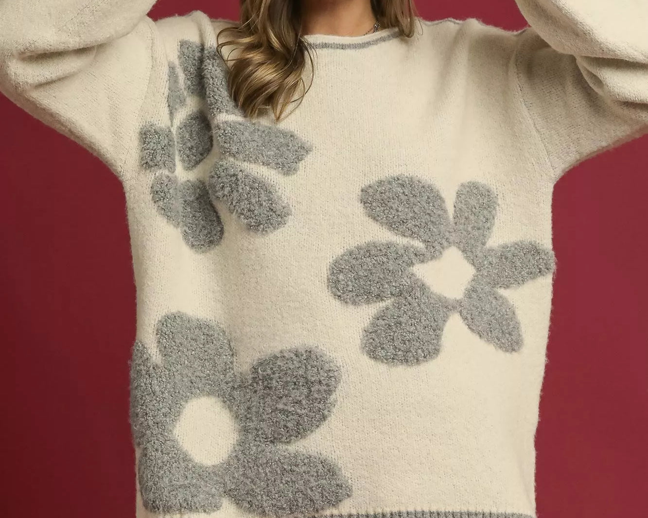 NEWYORKLISTED STYLE COLLECTION: Woman wearing a cream sweater with gray floral patterns against a red background
