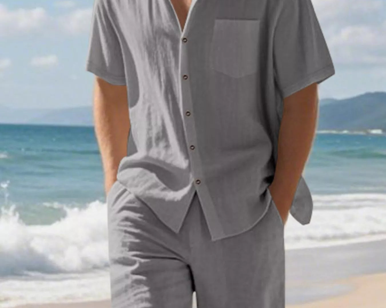 NEWYORKLISTED ATLAS MEN'S COLLECTION: Man wearing a gray shirt and shorts on a beach with ocean and sky in the background
