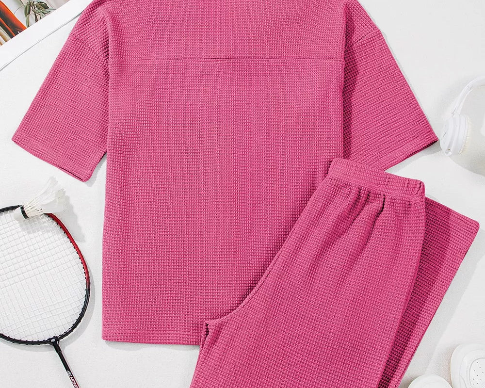 NEWYORKLISTED Comfort Collection: Pink textured shirt and pants set on a white surface with a badminton racket and shuttlecock.