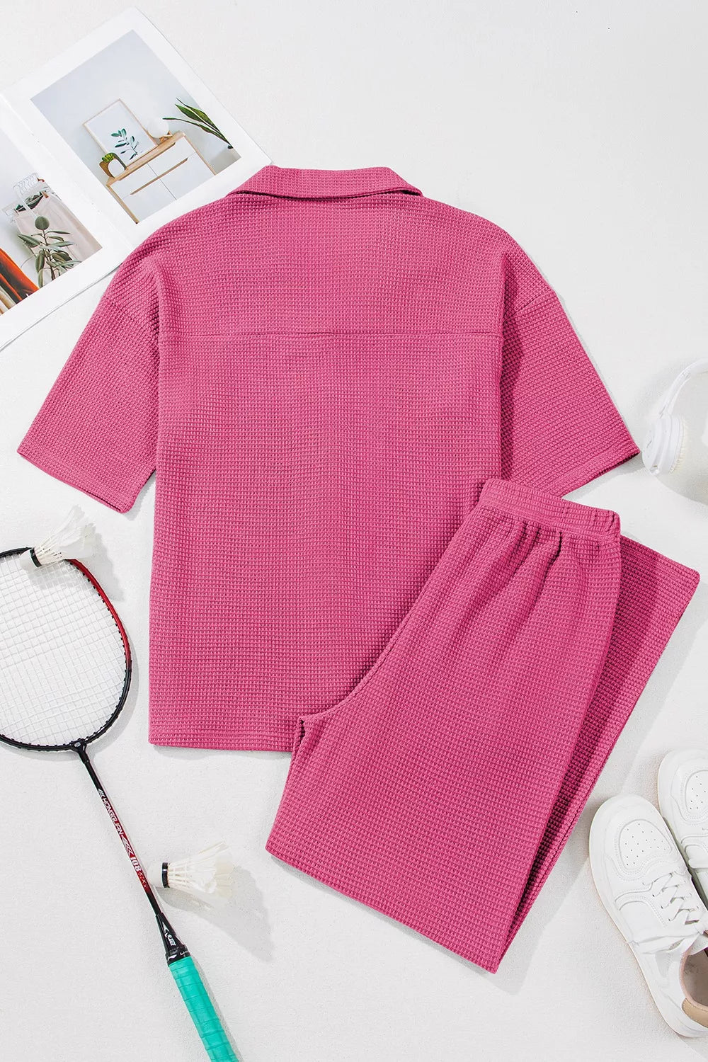 NEWYORKLISTED Comfort Collection: Pink textured shirt and pants set on a white surface with a badminton racket and shuttlecock.
