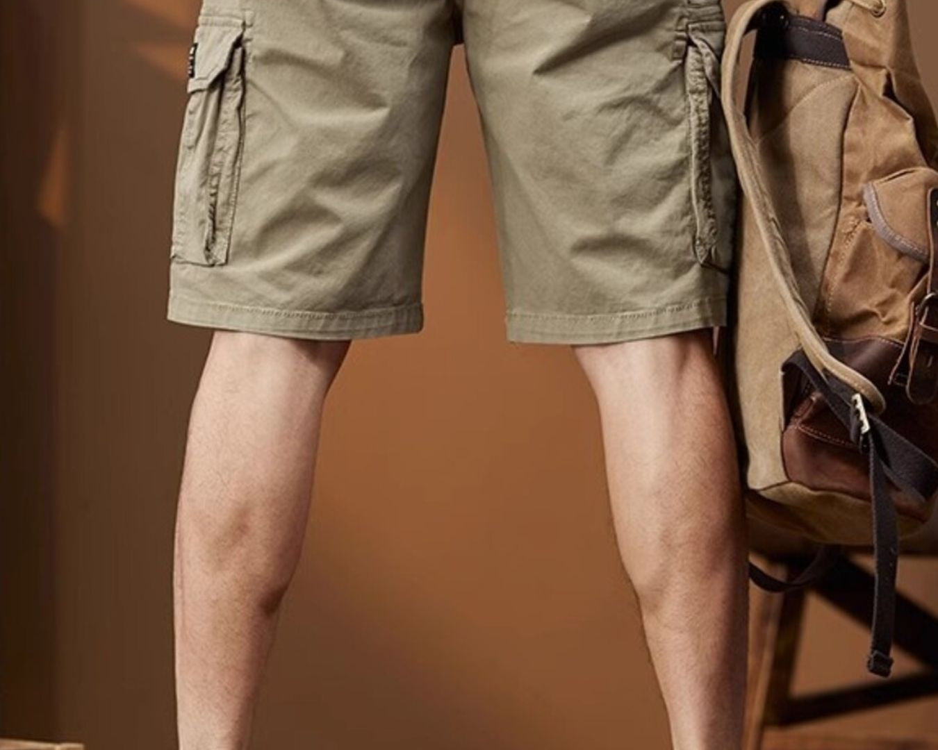 NEWYORKLISTED ATLAS MEN's COLLECTION: Person wearing beige cargo shorts with a brown backpack indoors.