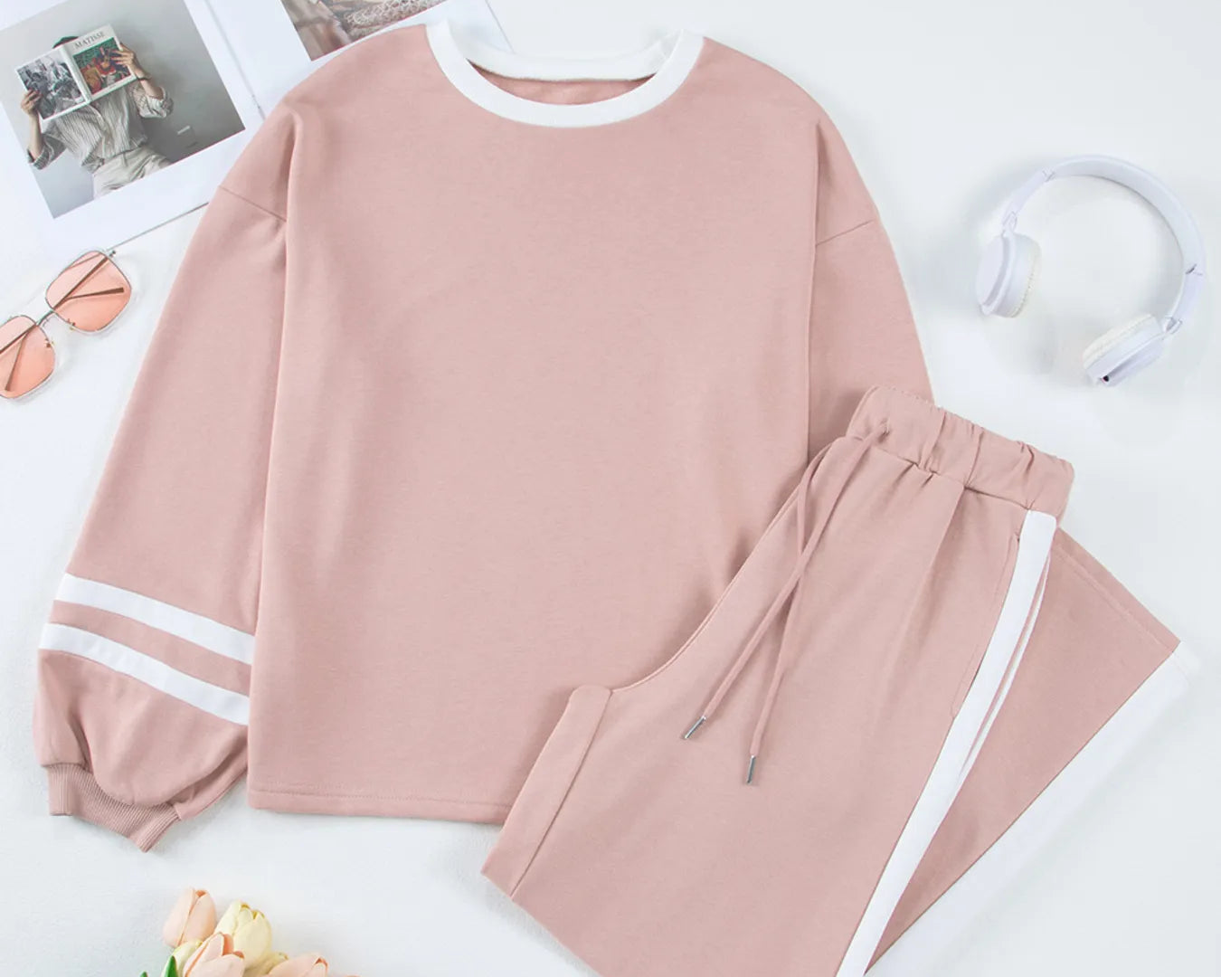 NEWYORKLISTED Comfort Collection: Pink sweatshirt and pants set on a white surface with flowers and photos.