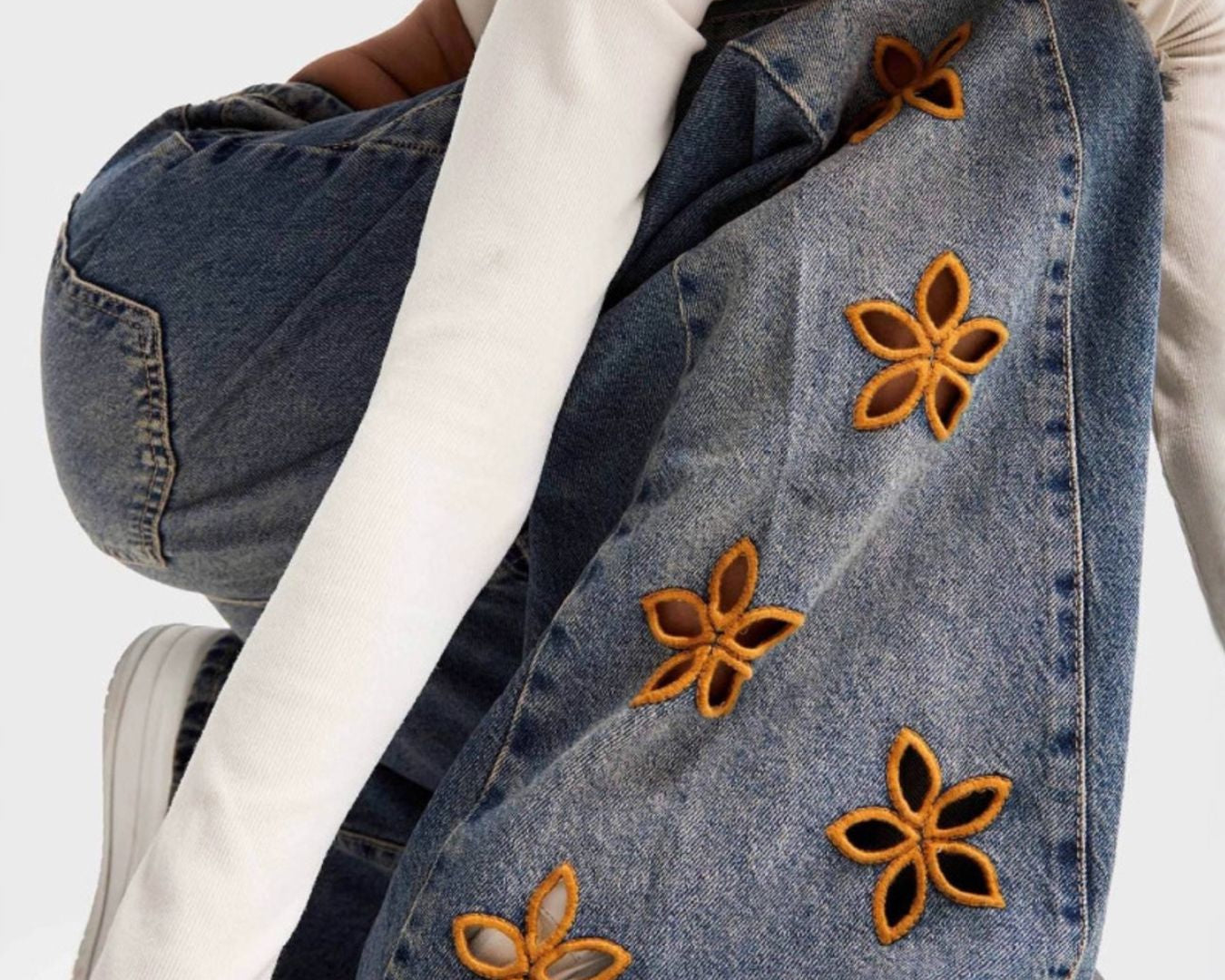 NEWYORKLISTED STYLE COLLECTION: Person wearing a denim jacket with floral embellishments on a white background