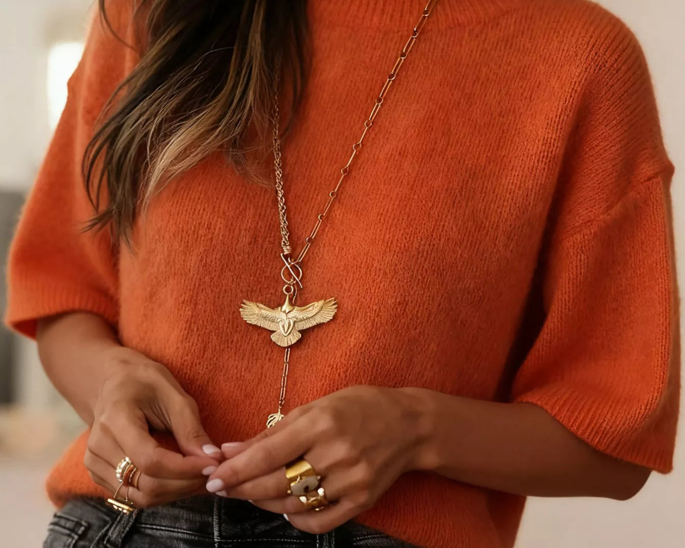 NEWYORKLISTED Style Collection: Person wearing an orange sweater and black pants with a gold necklace and rings.