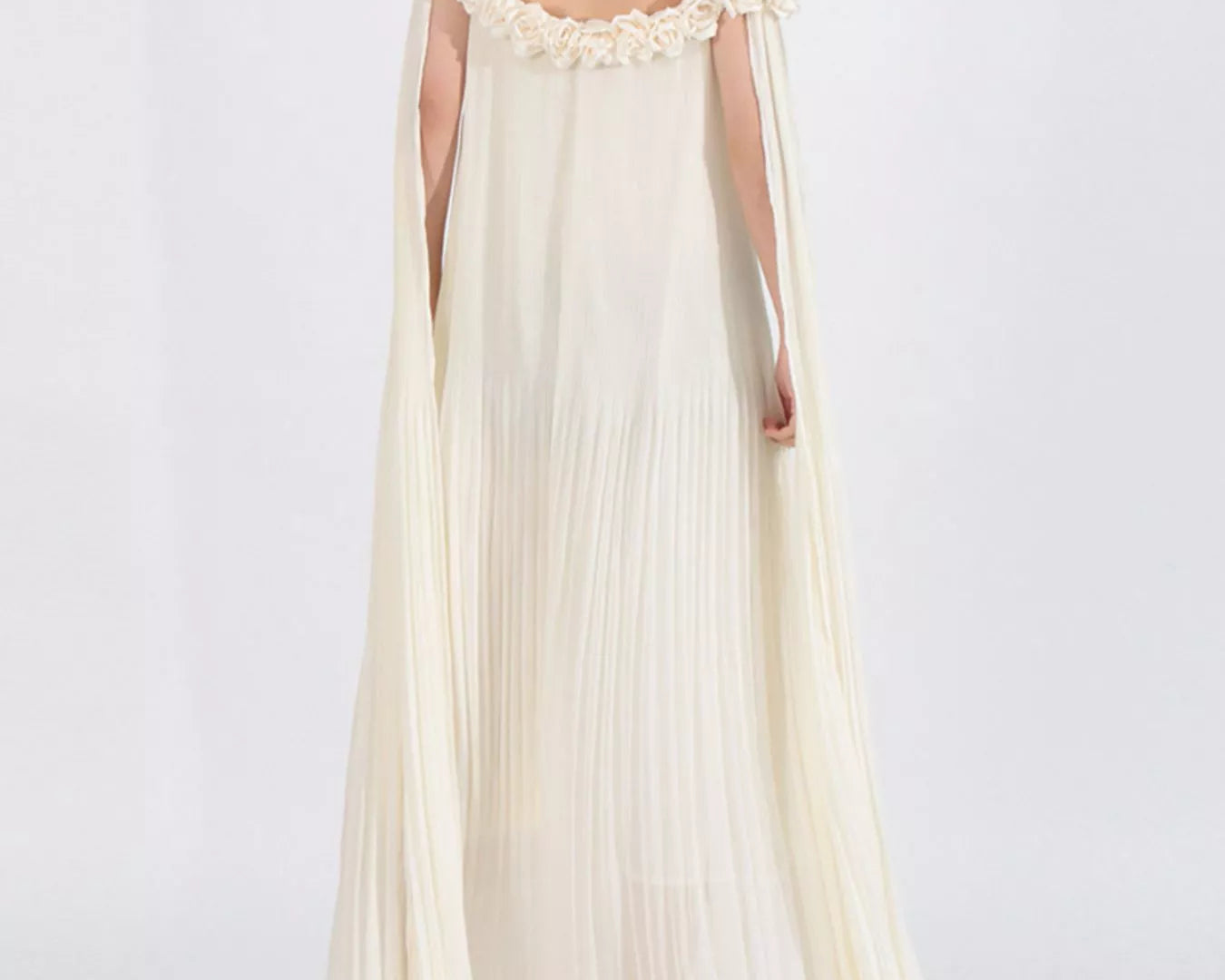 NEWYORKLISTED STYLE COLLECTION: Woman wearing a long, off-shoulder cream dress with floral details on a white background