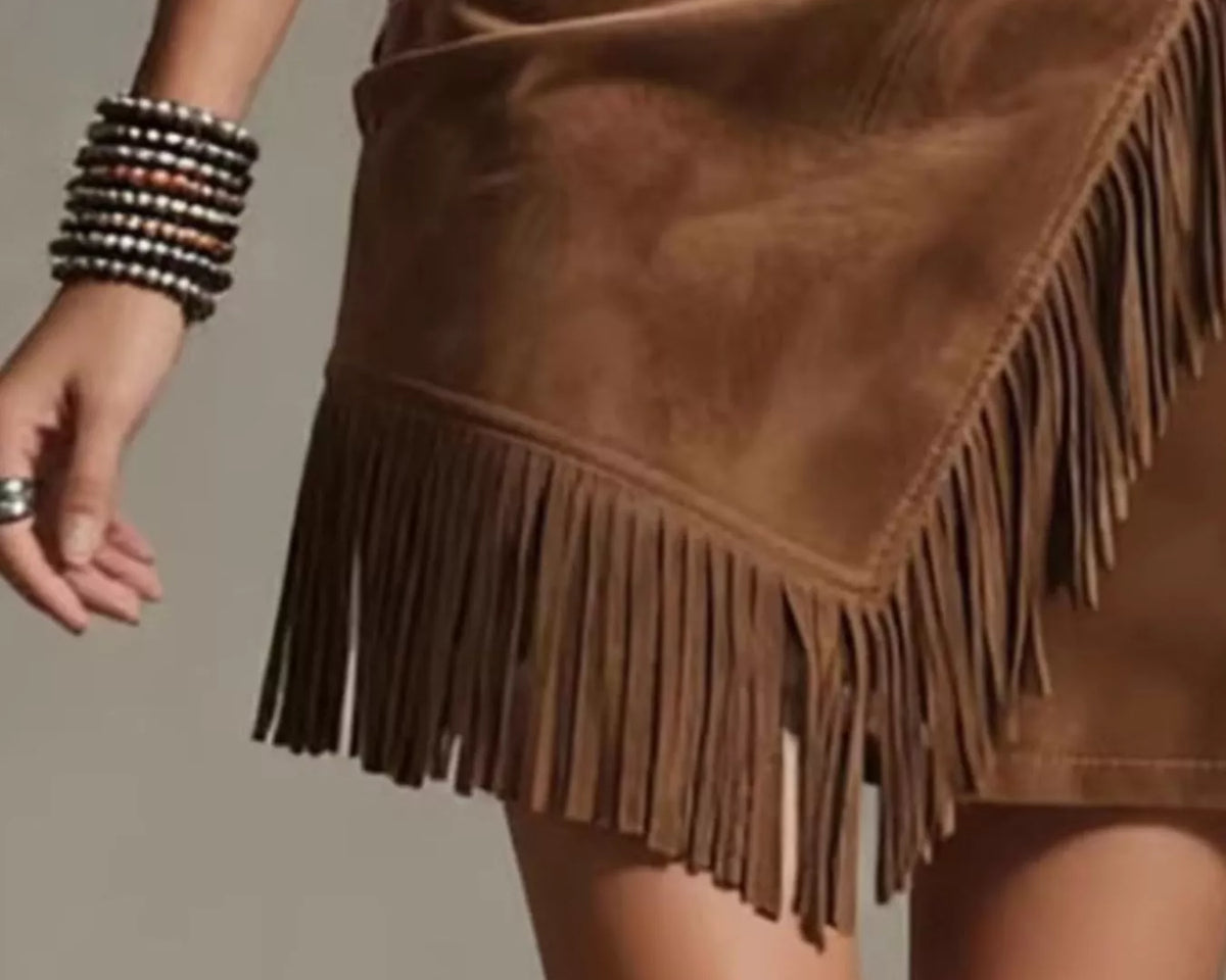 NEWYORKLISTED STYLE COLLECTION: A close-up of a brown suede fringe mini skirt worn by a model, showing the textured suede material, asymmetrical fringe hem, and side pockets.