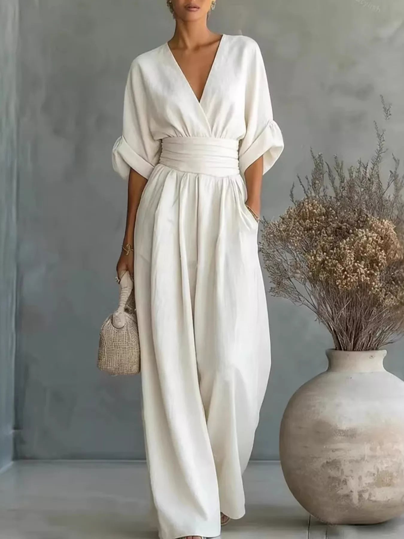 NEWYORKLISTED STYLE COLLECTION: Woman in a white dress standing next to a vase with dried flowers against a gray wall.