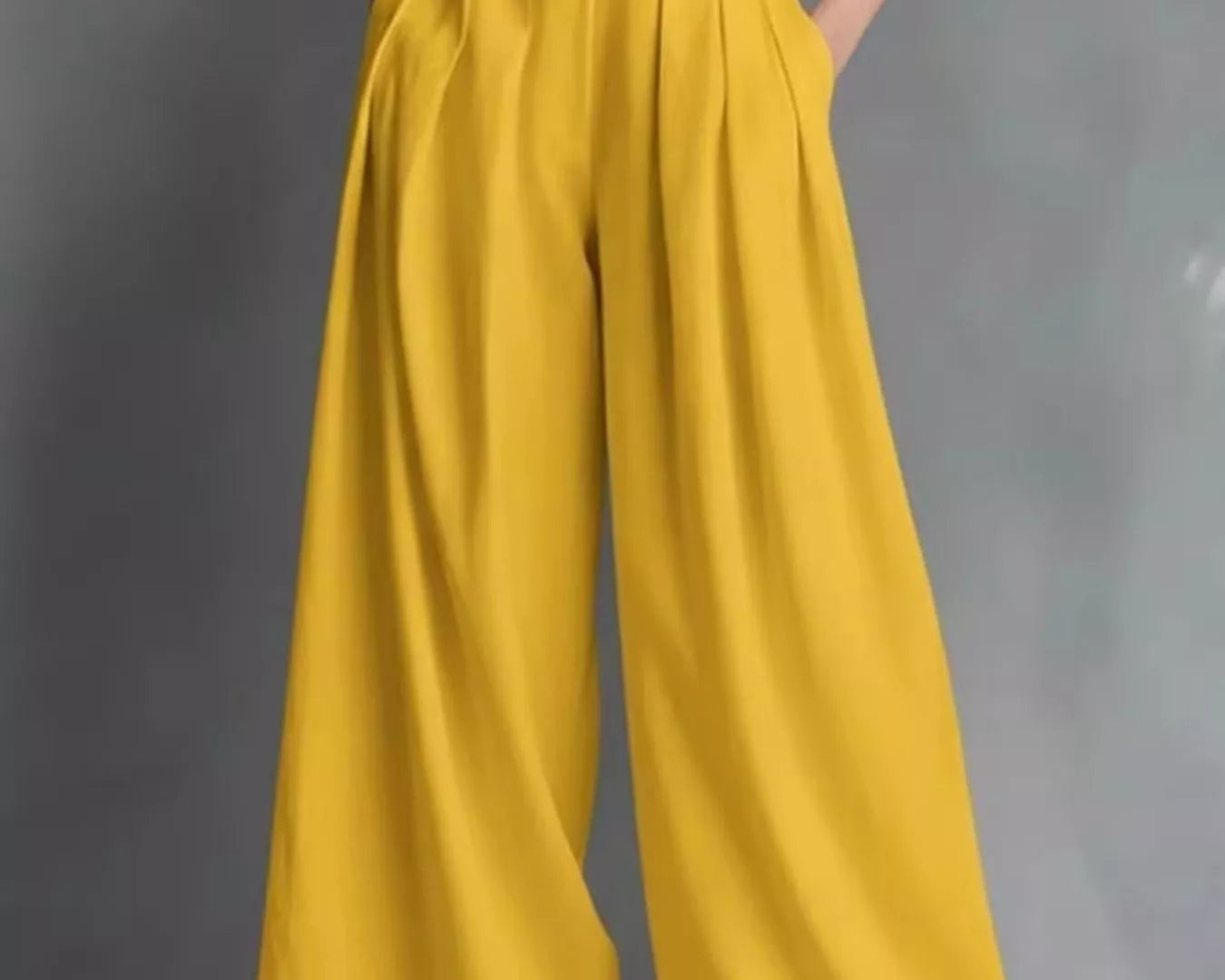 Mustard yellow wide-leg pants with a black top and white belt on a gray background