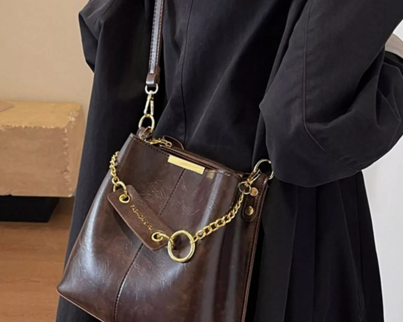 Brown leather handbag with gold chain strap held by a person wearing a black coat. New York Listed Style Collection