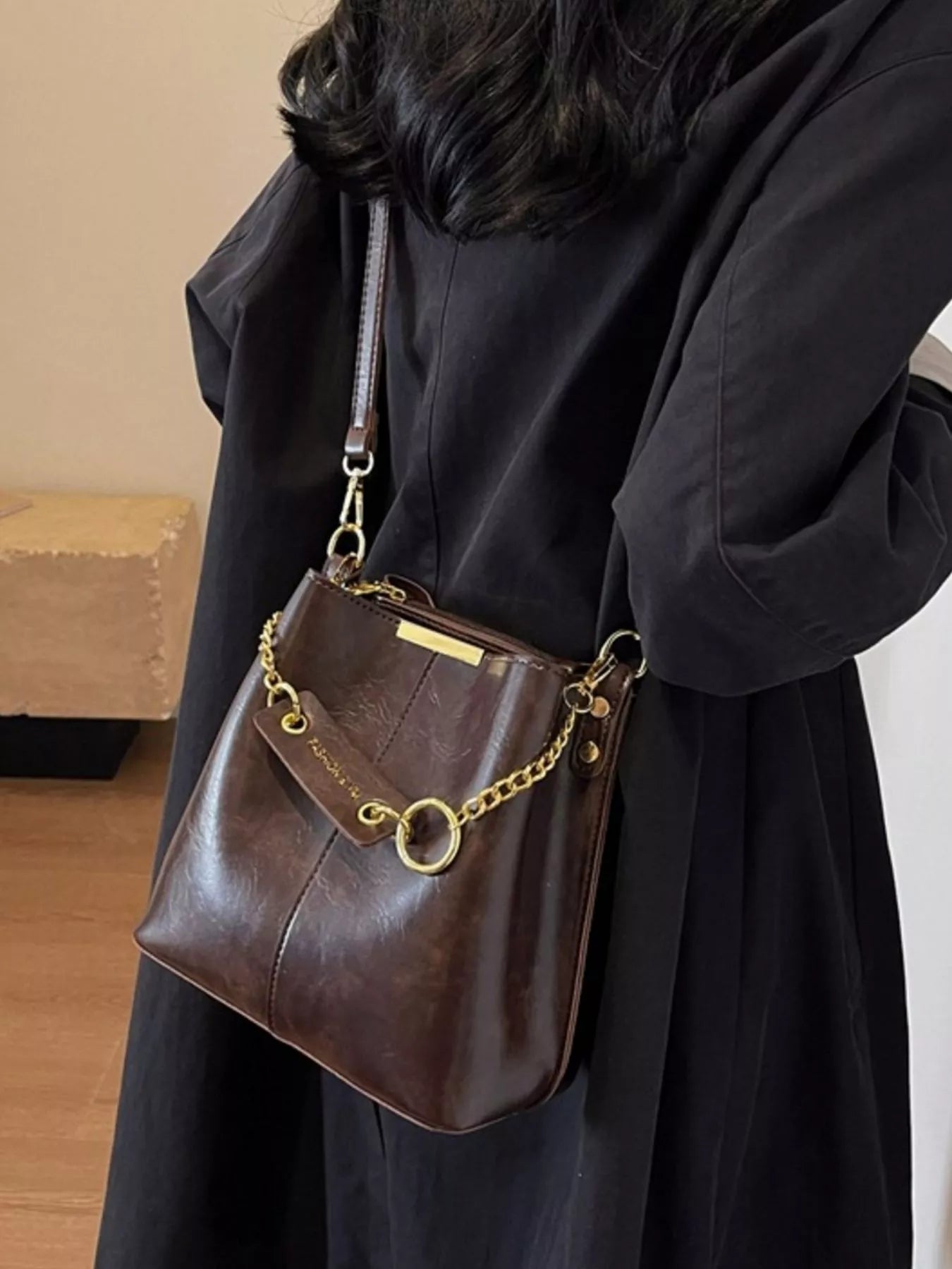 Brown leather handbag with gold chain strap held by a person wearing a black coat. New York Listed Style Collection