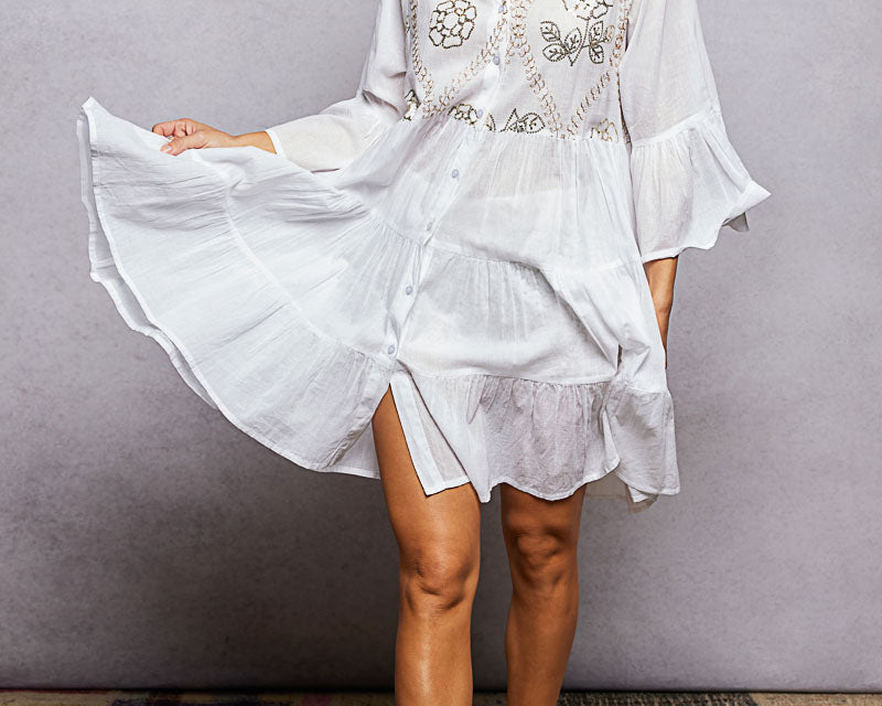 NEWYORKLISTED STYLE COLLECTION: Woman wearing a white embroidered dress with yellow cowboy boots on a textured floor.