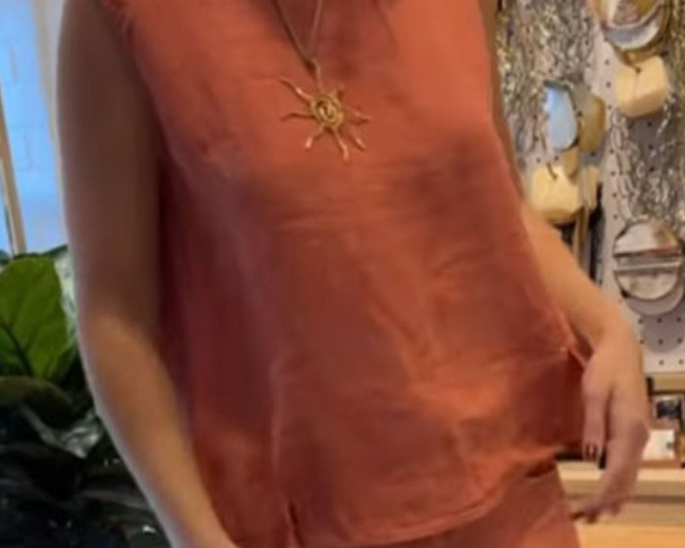 NEWYORKLISTED COMFORT COLLECTION: Person wearing a sleeveless orange top with a sun pendant necklace in a store setting.