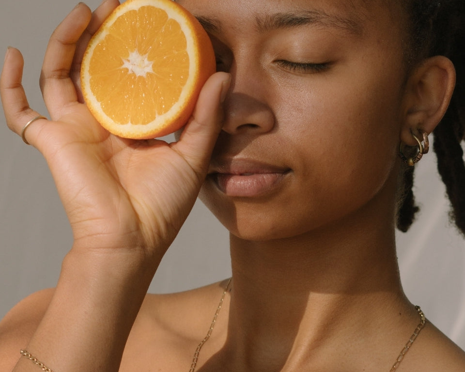 NEWYORKLISTED COSMETIC COLLECTION: Grow Hair Oil, Woman holding a sliced orange to her face against a neutral background