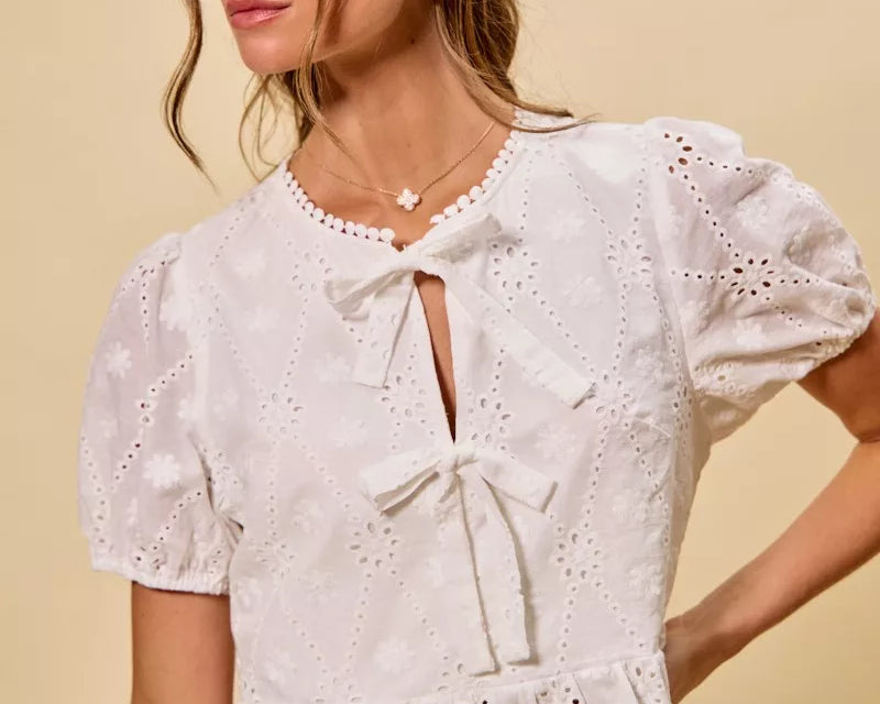 NEWYORKLISTED STYLE COLLECTION: Woman wearing a white embroidered blouse with puff sleeves against a beige background