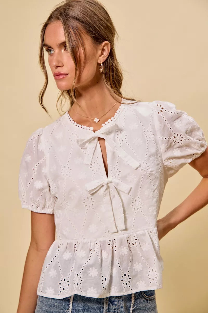 NEWYORKLISTED STYLE COLLECTION: Woman wearing a white embroidered blouse with puff sleeves against a beige background