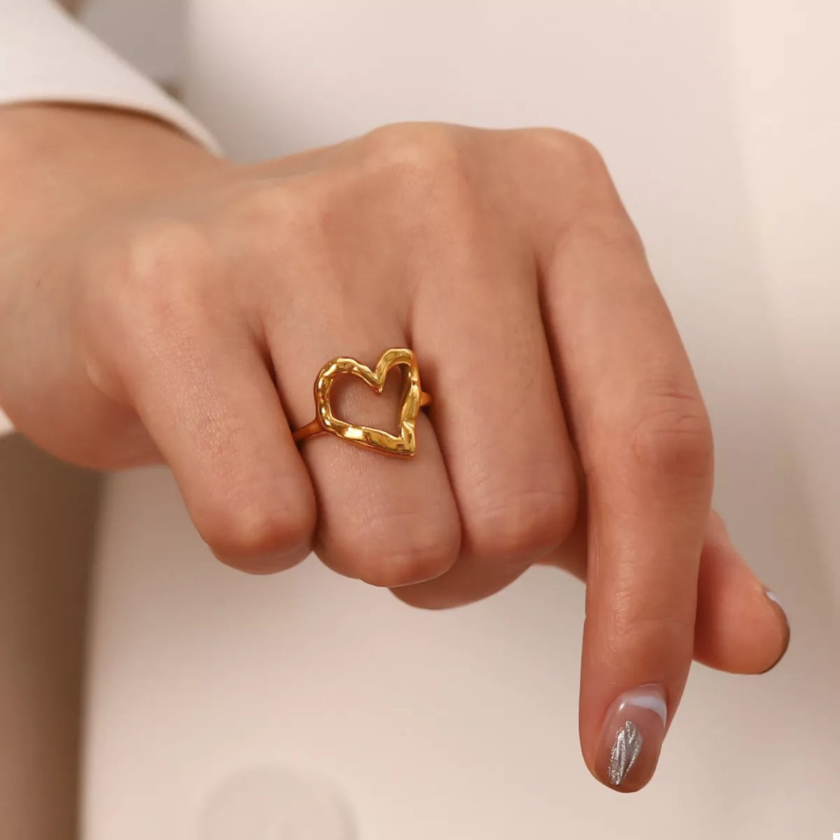 NYLD Glamour Collection by NEWYORKLISTED: Gold heart-shaped ring on a finger against a neutral background