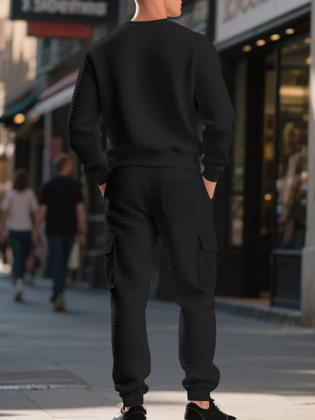 NEWYORKLISTED ATLAS MEN'S COLLECTION: A man viewed from behind wearing a matching black textured knit crewneck sweatshirt and cargo jogger pants on a city sidewalk.