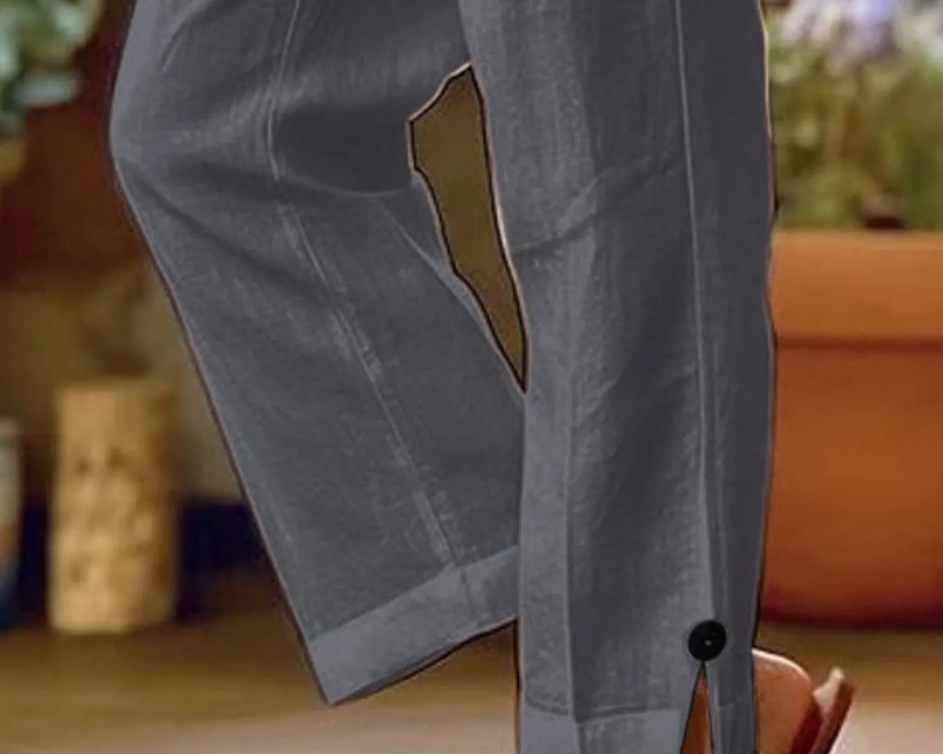 NEWYORKLISTED STYLE COLLECTION: A close-up of a person wearing gray wide-leg cropped pants with a button detail at the hem and a side slit, paired with tan sandals in an outdoor patio setting.