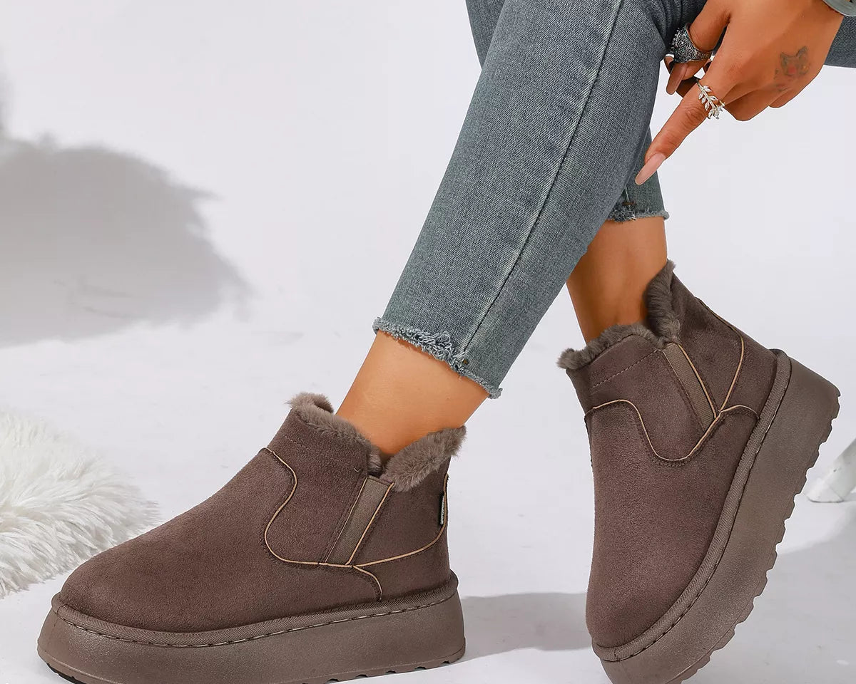 NEWYORKLISTED SHOE COLLECTION: A person wearing taupe-brown platform Chelsea-style ankle boots with fuzzy shearling lining, paired with gray skinny jeans, shown against a white studio background.