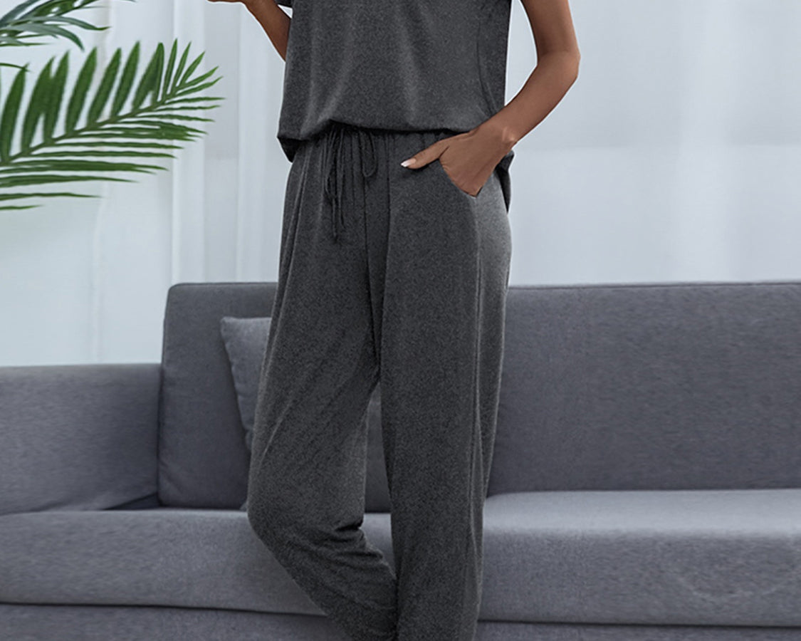 NEWYORKLISTED Intimate Apparel: Person wearing a gray lounge set sitting on a gray couch with a white wall and plant in the background.