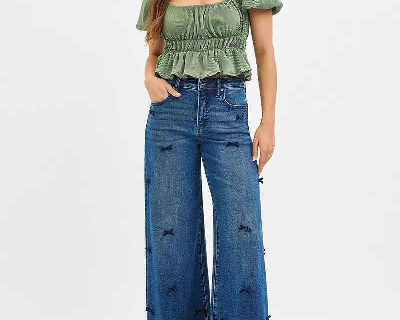 NEWYORKLISTED STYLE COLLECTION: Woman wearing a green top and blue jeans with distressed details on a white background