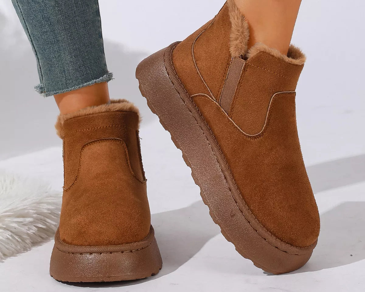 NEWYORKLISTED SHOE COLLECTION: A pair of women's brown suede ankle boots with plush faux-fur lining, shown on a model wearing blue jeans against a clean white background.