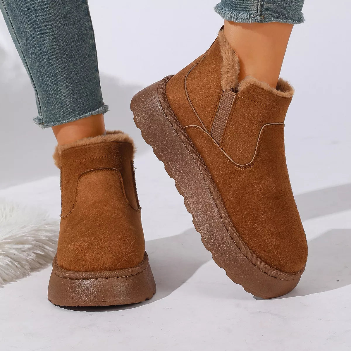 NEWYORKLISTED SHOE COLLECTION: A pair of women's brown suede ankle boots with plush faux-fur lining, shown on a model wearing blue jeans against a clean white background.
