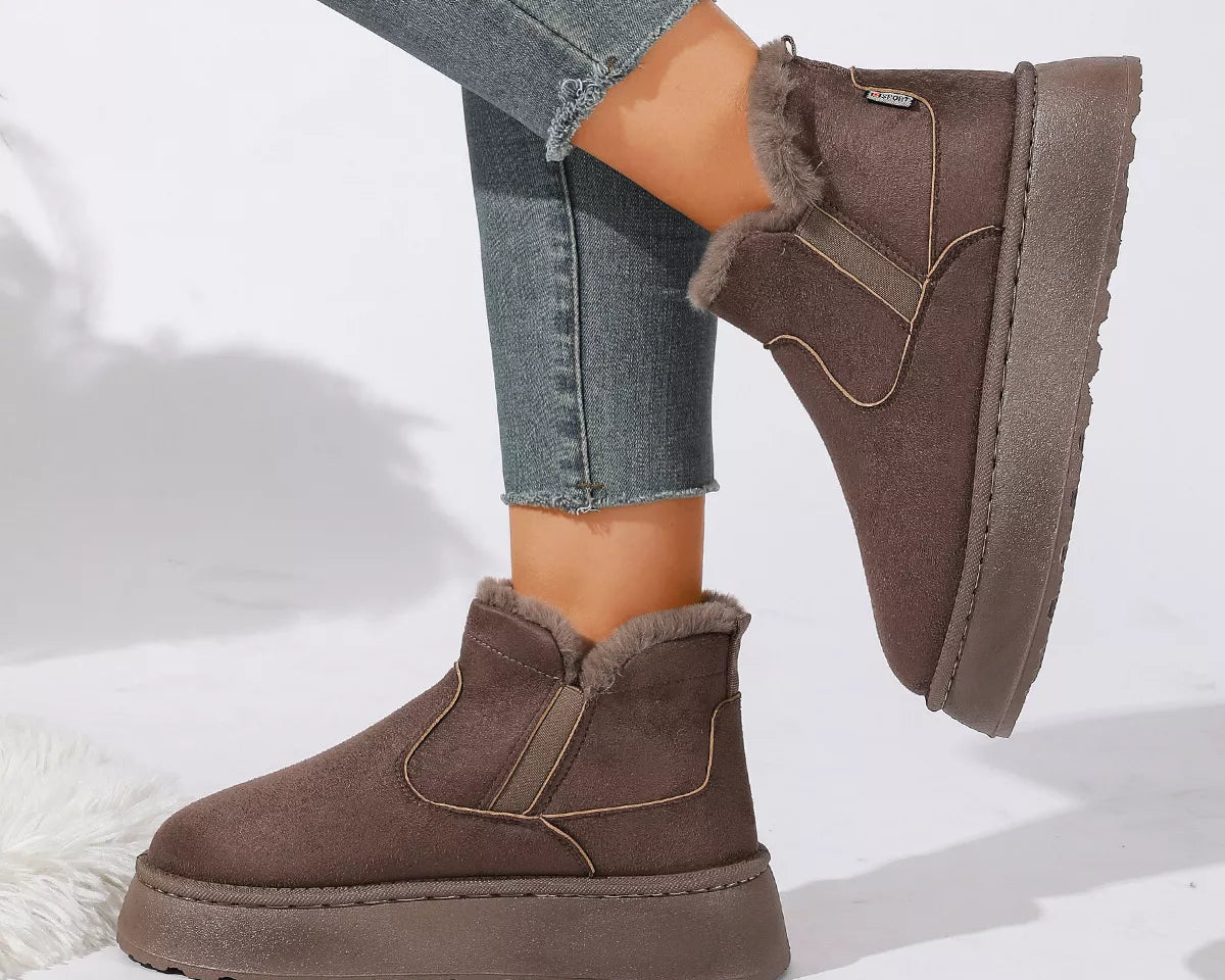 NEWYORKLISTED SHOE COLLECTION: A pair of women's mid-calf slip-on boots in taupe brown faux suede with a fuzzy lining, styled with frayed blue jeans on a white studio background.
