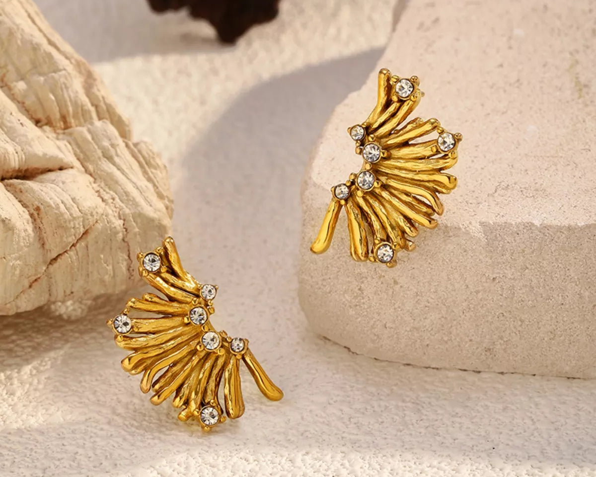 NYLD Glamour Collection by NEWYORKLISTED: Gold leaf-shaped earrings with rhinestones on a textured beige surface