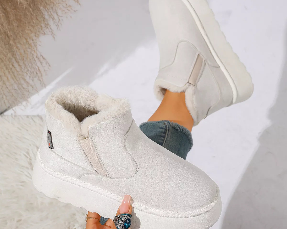 NEWYORKLISTED SHOE COLLECTION: A pair of off-white winter slip-on boots with plush faux-fur lining, shown worn with blue jeans and held by a hand against a bright, modern background.