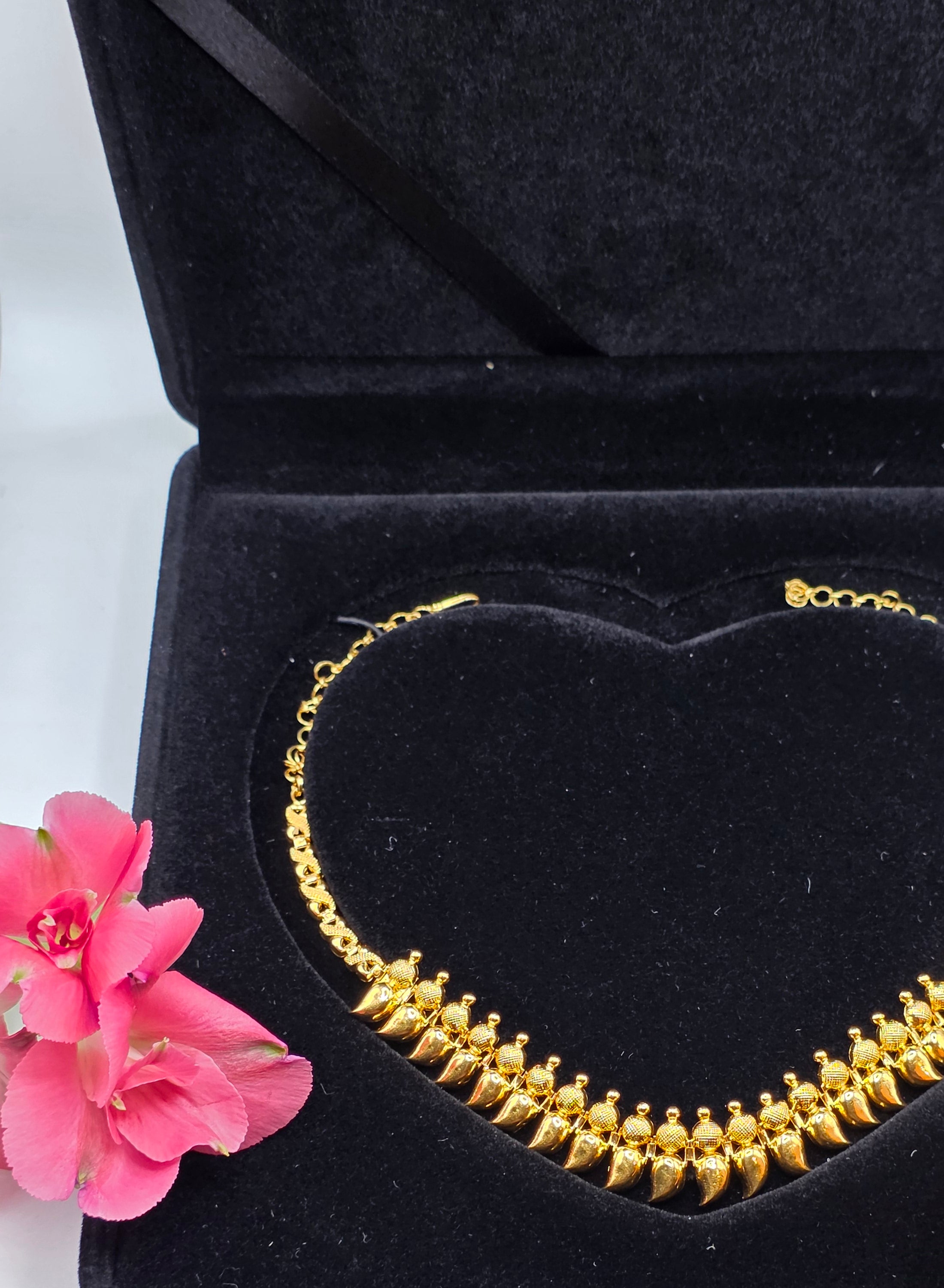 NEWYORKLISTED 22k gold necklace in a black jewelry box with pink and orange flowers on a white background