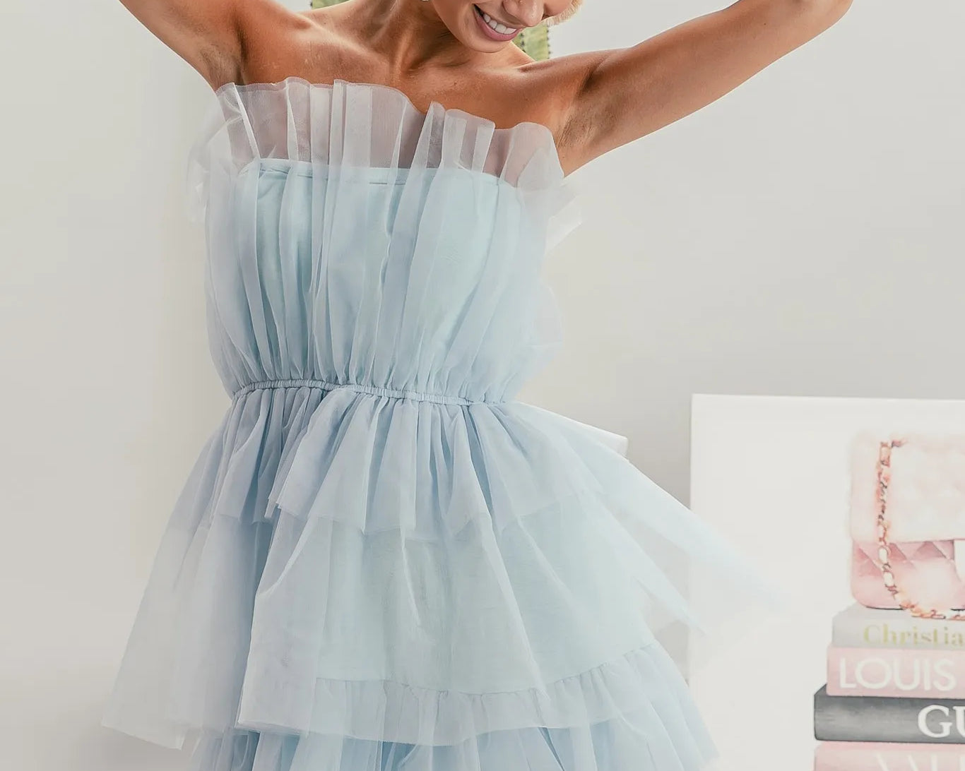 NEWYORKLISTED STYLE COLLECTION: Sleeveless Layered Organza Dress: Woman wearing a light blue strapless dress with a white background and books in the background.
