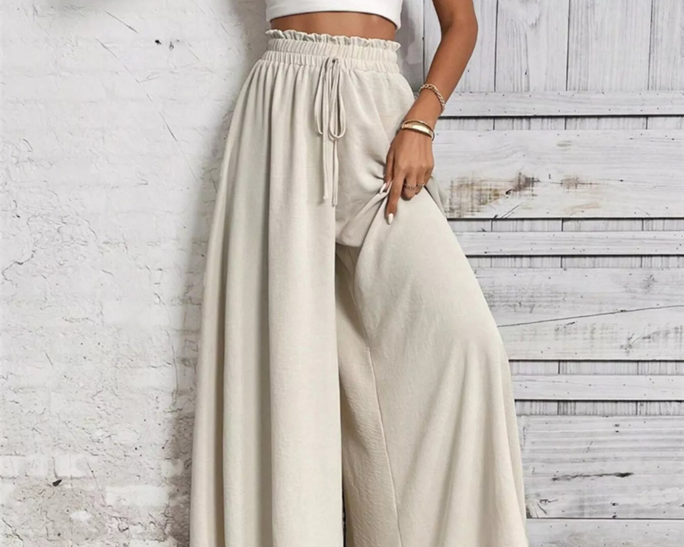 NEWYORKLISTED: Woman wearing a white top and beige wide-leg pants against a light wooden panel background