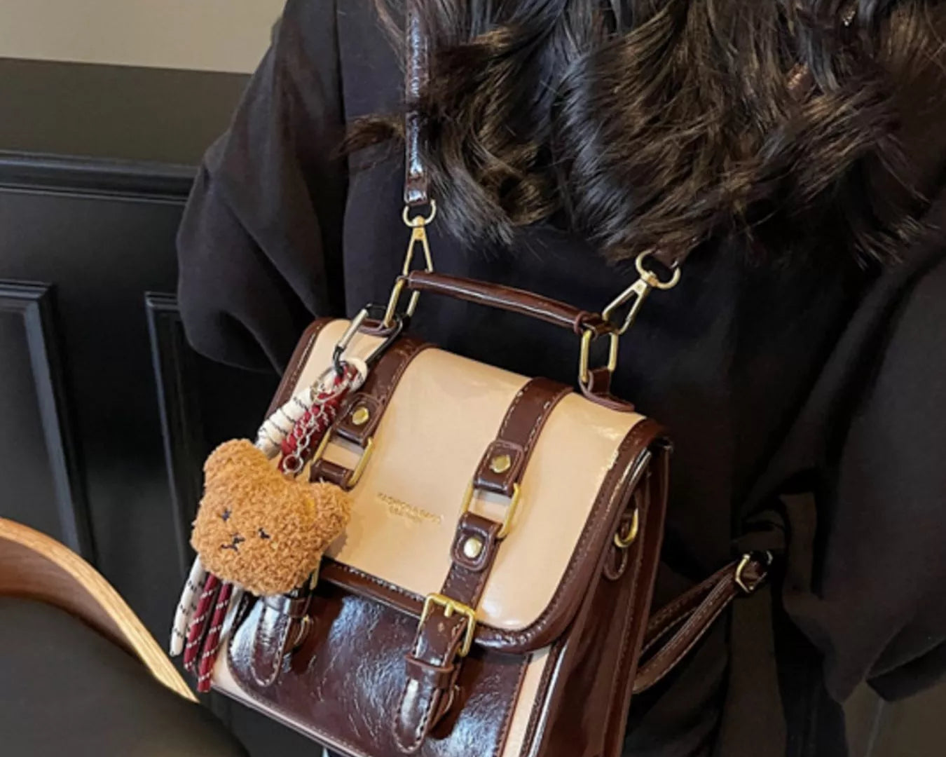 NEWYORKLISTED STYLE COLLECTION: Person holding a brown and beige handbag with a teddy bear keychain indoors.