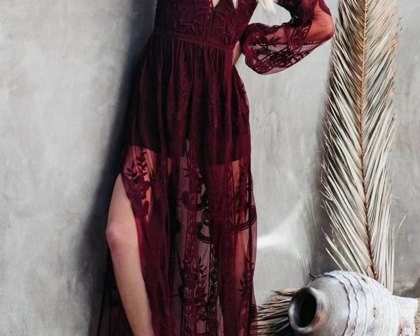 NEWYORKLISTED STYLE COLLECTION: Woman wearing a burgundy lace dress against a textured wall.