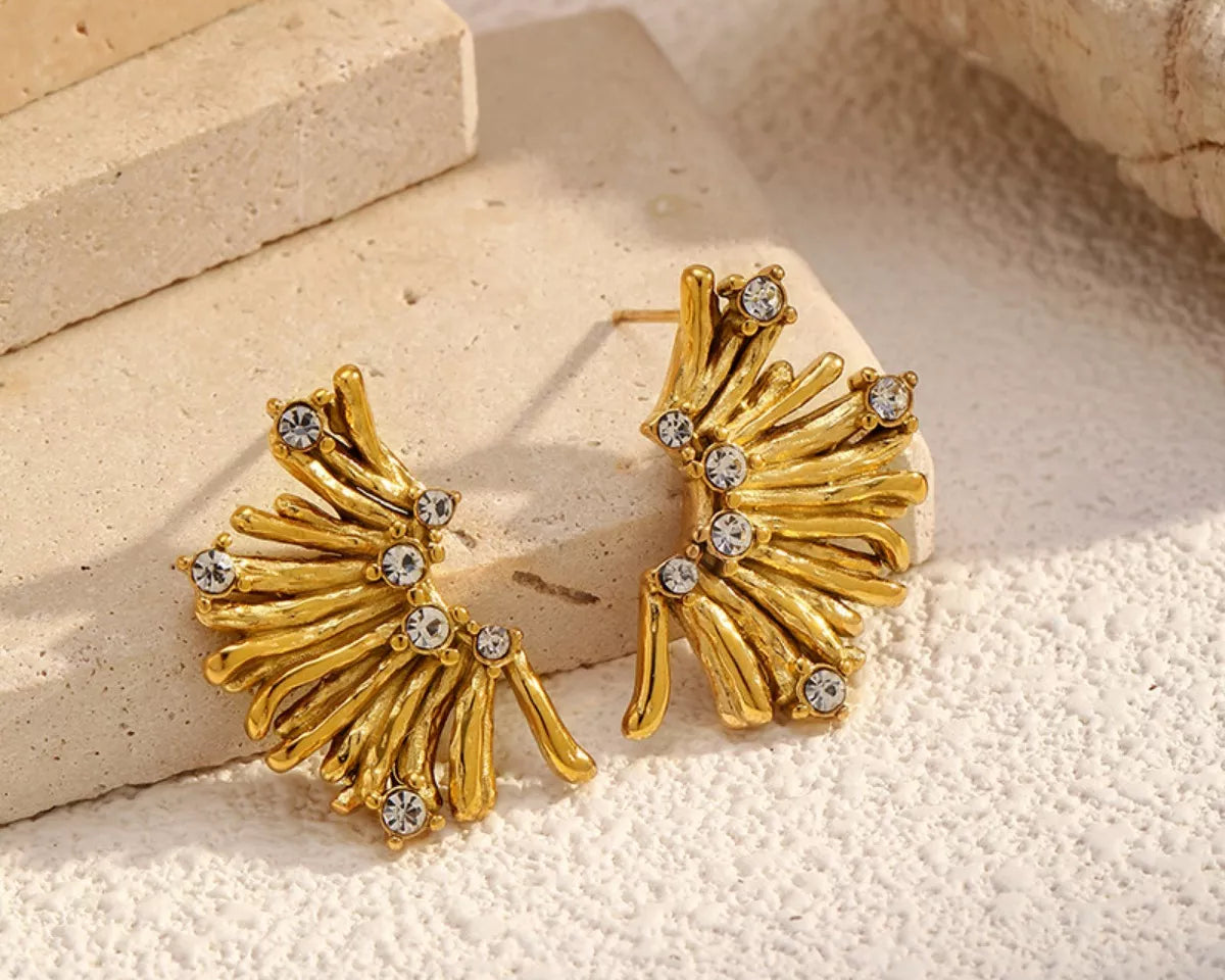 NYLD Glamour Collection by NEWYORKLISTED: Gold earrings with fan-like design and embedded stones on a textured surface