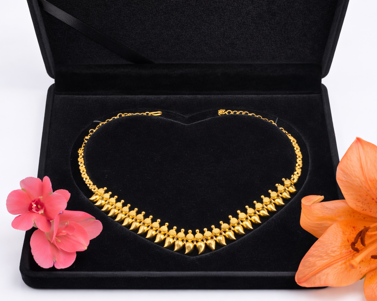 NEWYORKLISTED Valentine's Day: 22K Gold necklace in a black jewelry box with pink and orange flowers on a white background