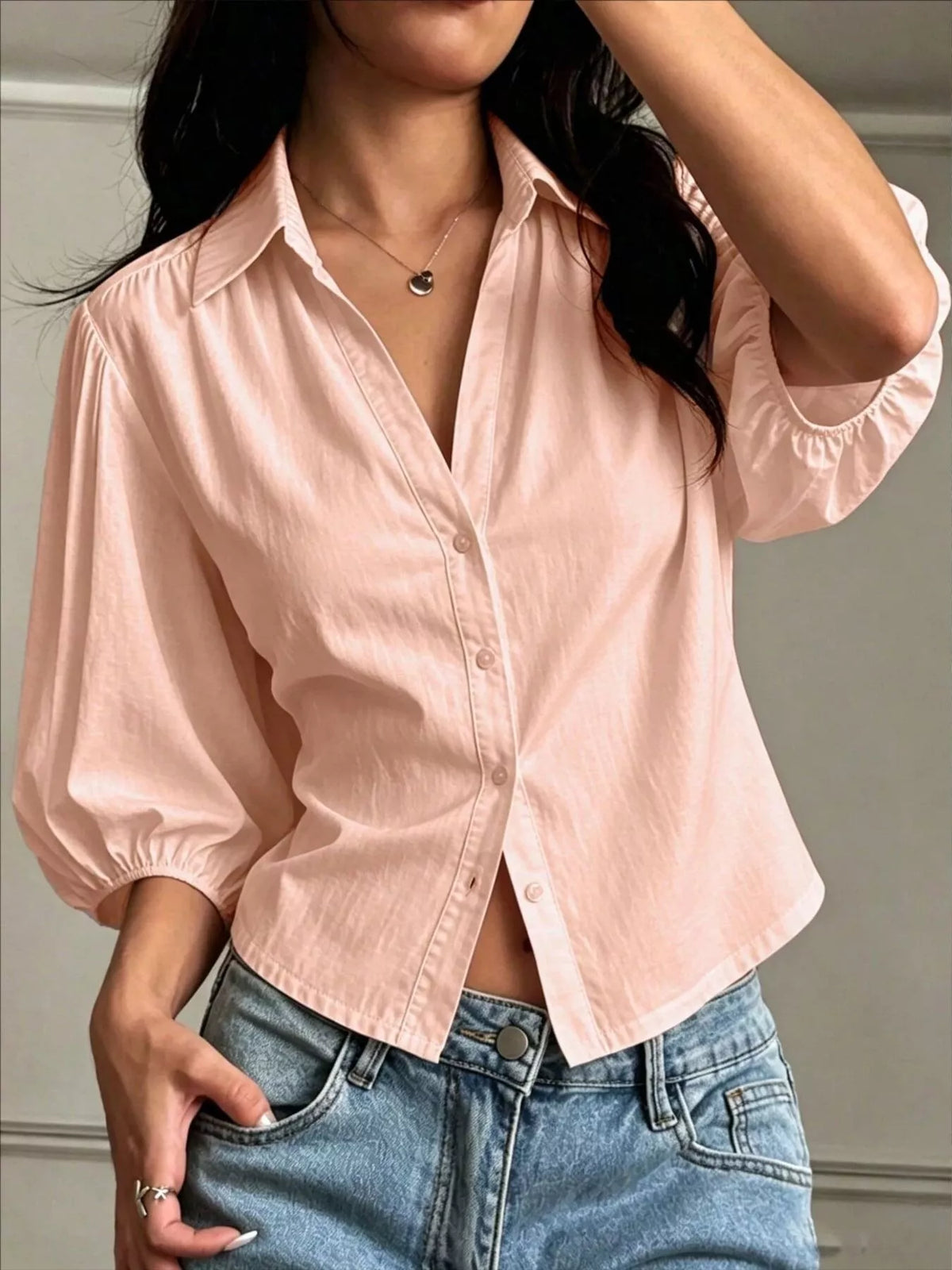 NEWYORKLISTED STYLE COLLECTION: A woman wearing a light pink short-sleeve button-up shirt with gathered puff sleeves and blue jeans, shown from the neck down in an indoor setting.