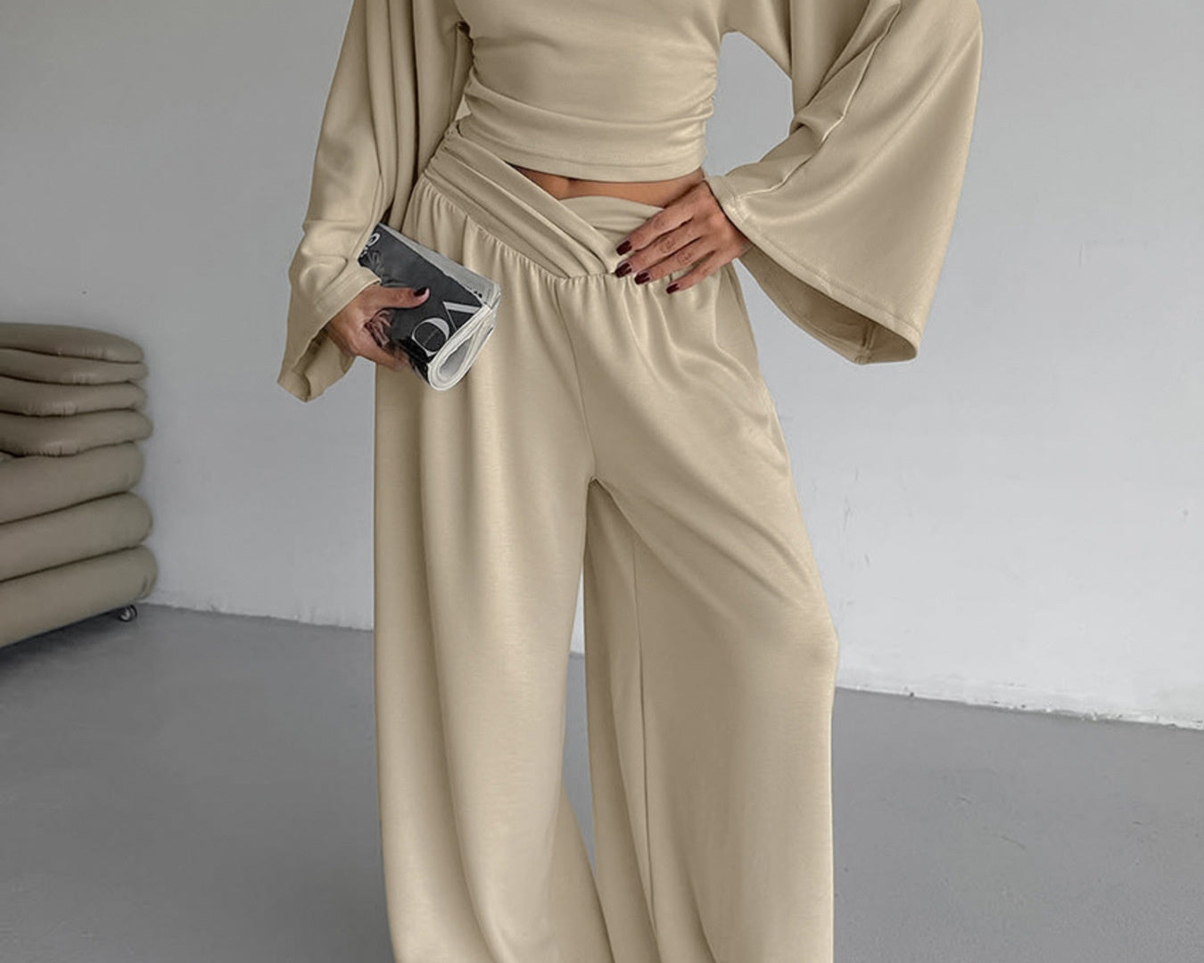 NEWYORKLISTED STYLE COLLECTION: Person wearing a beige outfit with wide sleeves and pants, holding a phone.