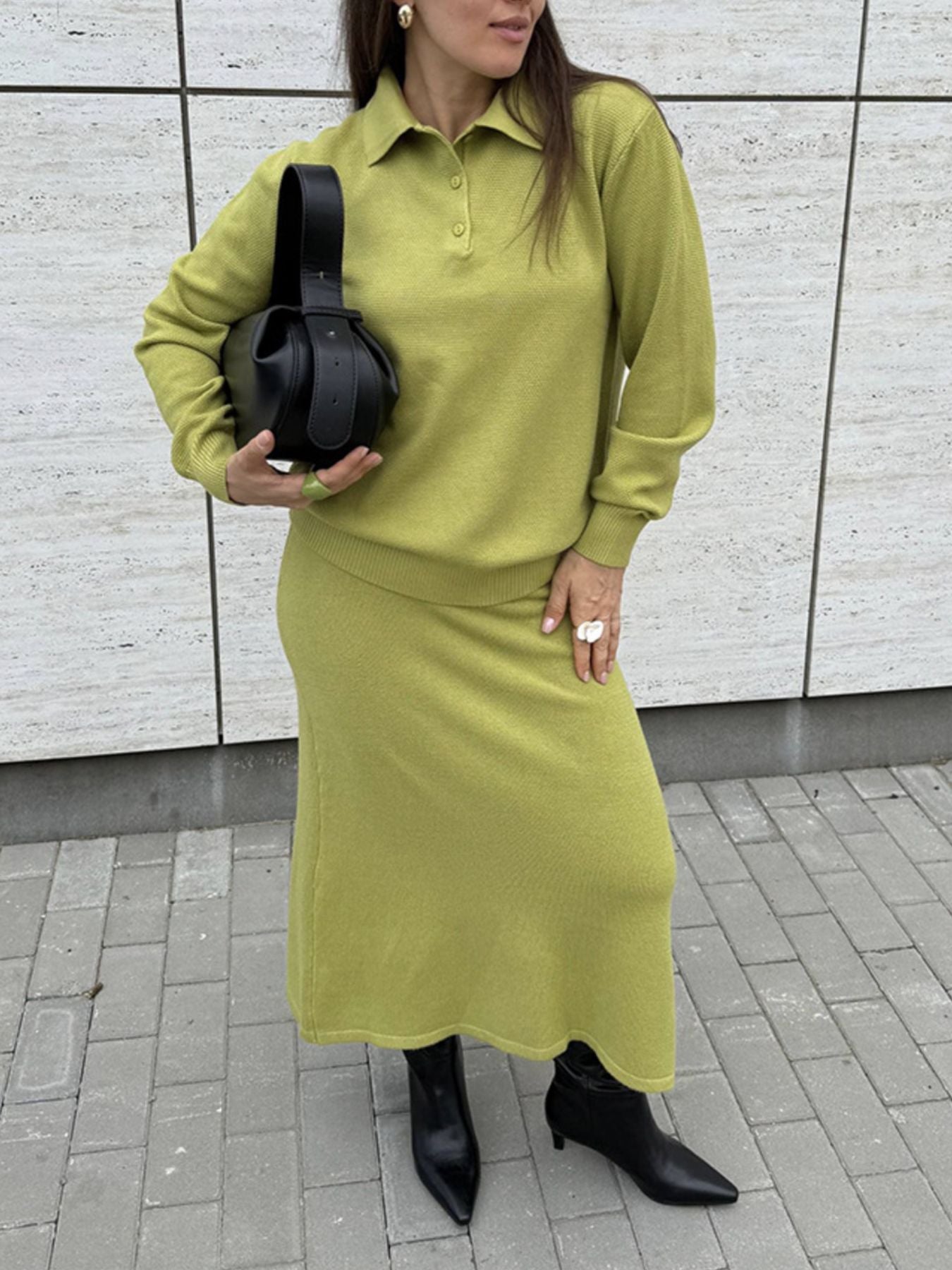 NEWYORKLISTED Comfort Collection: Woman wearing a green outfit with a black bag against a light-colored wall.
