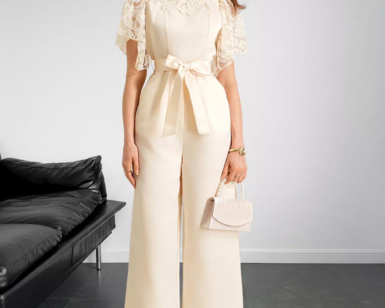 NEWYORKLISTED STYLE COLLECTION: Woman in a cream lace top and wide-leg pants holding a handbag against a plain background