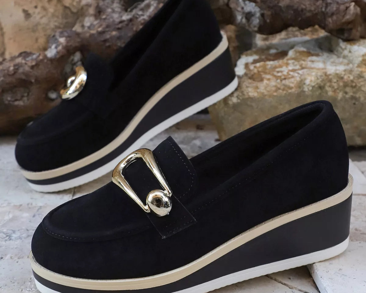 NEWYORKLISTED SHOE COLLECTION: Black loafers with gold buckles on a stone surface