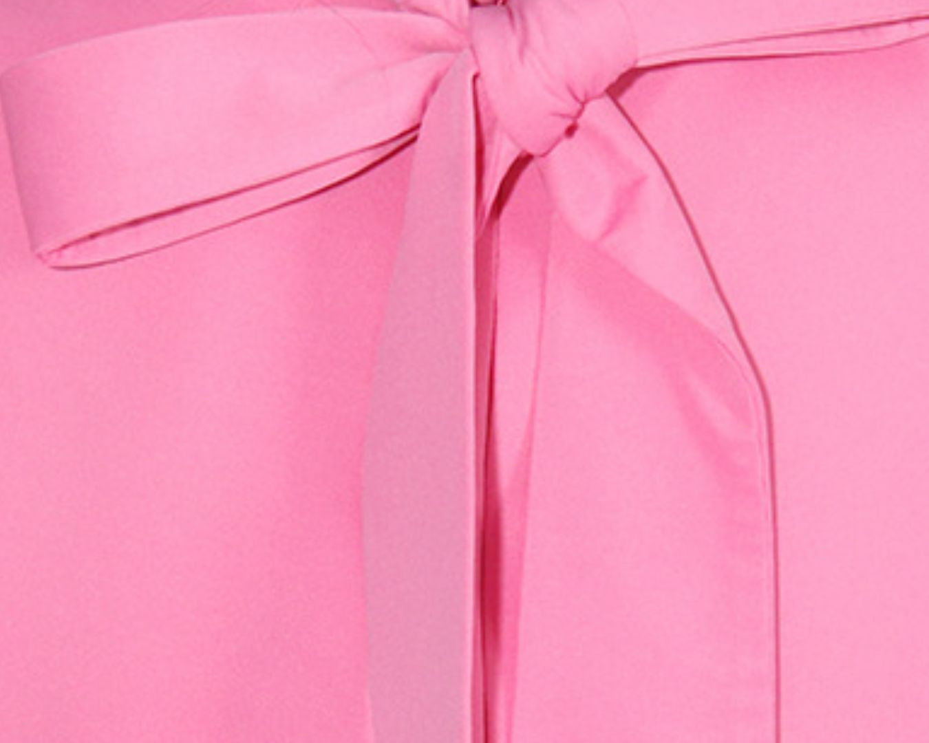 NEWYORKLISTED STYLE COLLECTION: Close-up of a pink blouse with a large bow detail on a white background