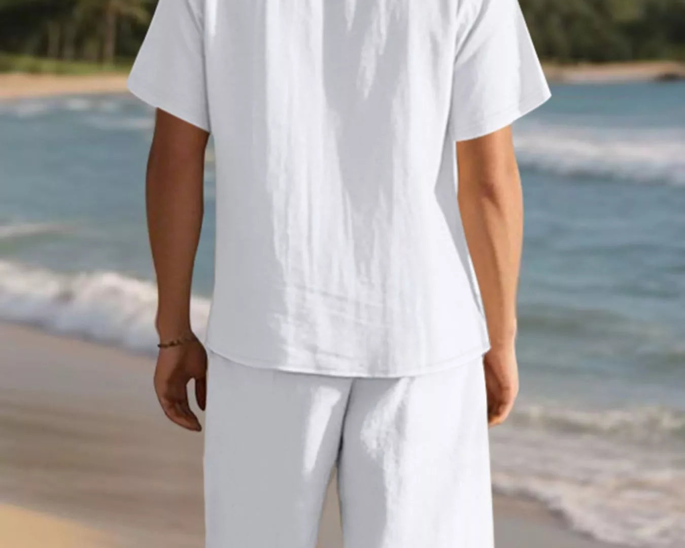 NEWYORKLISTED ATLAS MEN'S COLLECTION: Person wearing a white shirt and shorts on a beach with mountains in the background